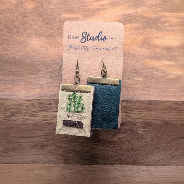 Rectangle hand embroidered fabric medium size earrings with felt core and pleather back. Front is a hand embroidered potted plant on a shelf, back is a forest green pleather. Coupled with a b